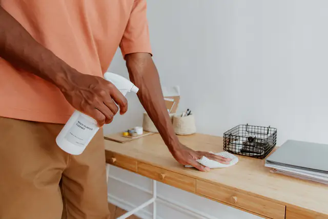 Cleaner wiping down an office desk with spray and cloth during daily office cleaning
