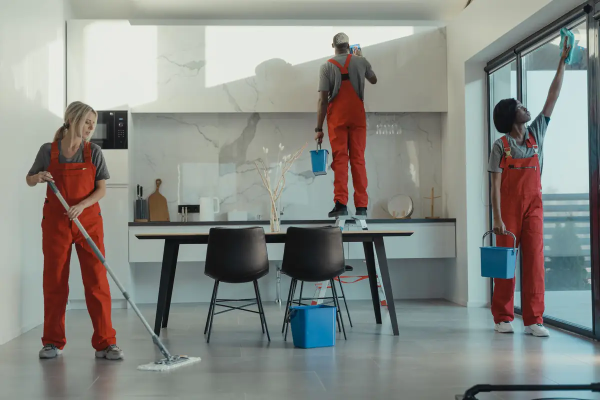 Office cleaning team mopping the floor, wiping cabinets and cleaning glass in a corporate pantry