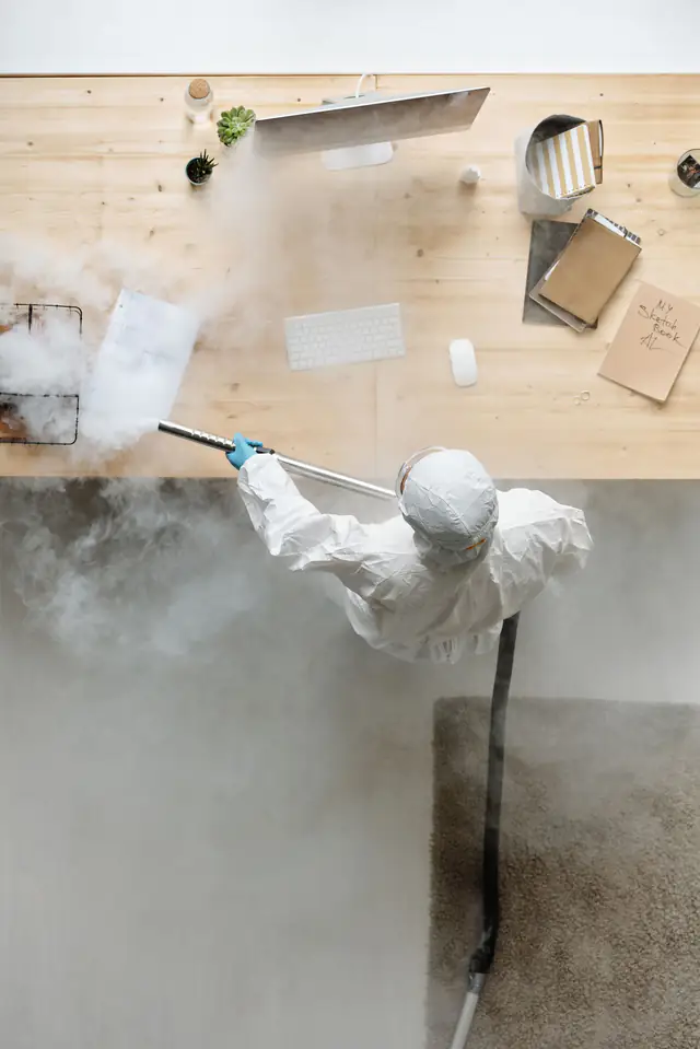 Technician in protective suit disinfecting office desks