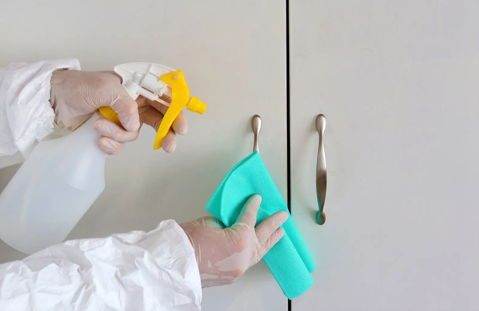 Gloved hands disinfecting cabinet handles, a high-touch surface targeted during home sanitization