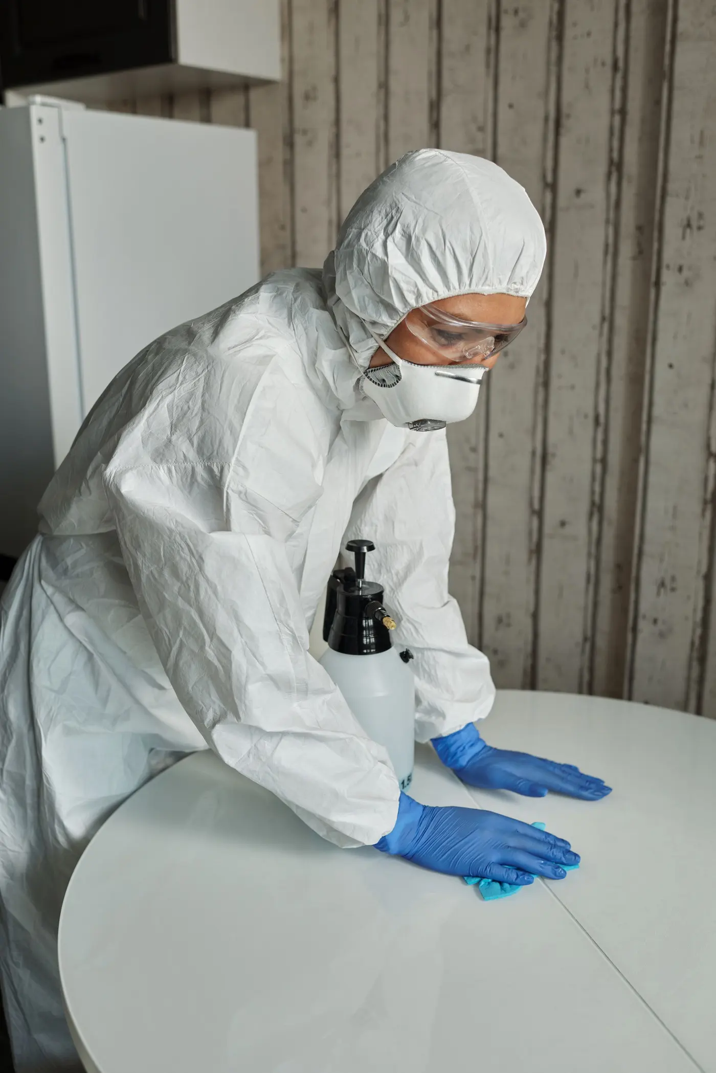 Technician in full PPE disinfecting a home surface with a sanitizing spray during a home sanitization service in Delhi NCR