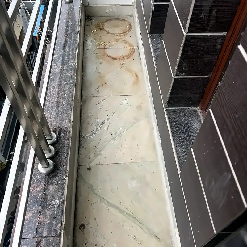 Rust rings and embedded dirt on a Delhi balcony floor before professional cleaning