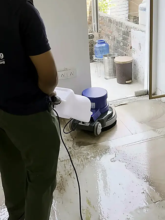 Technician using a single-disc rotary machine with solution tank on a tiled floor