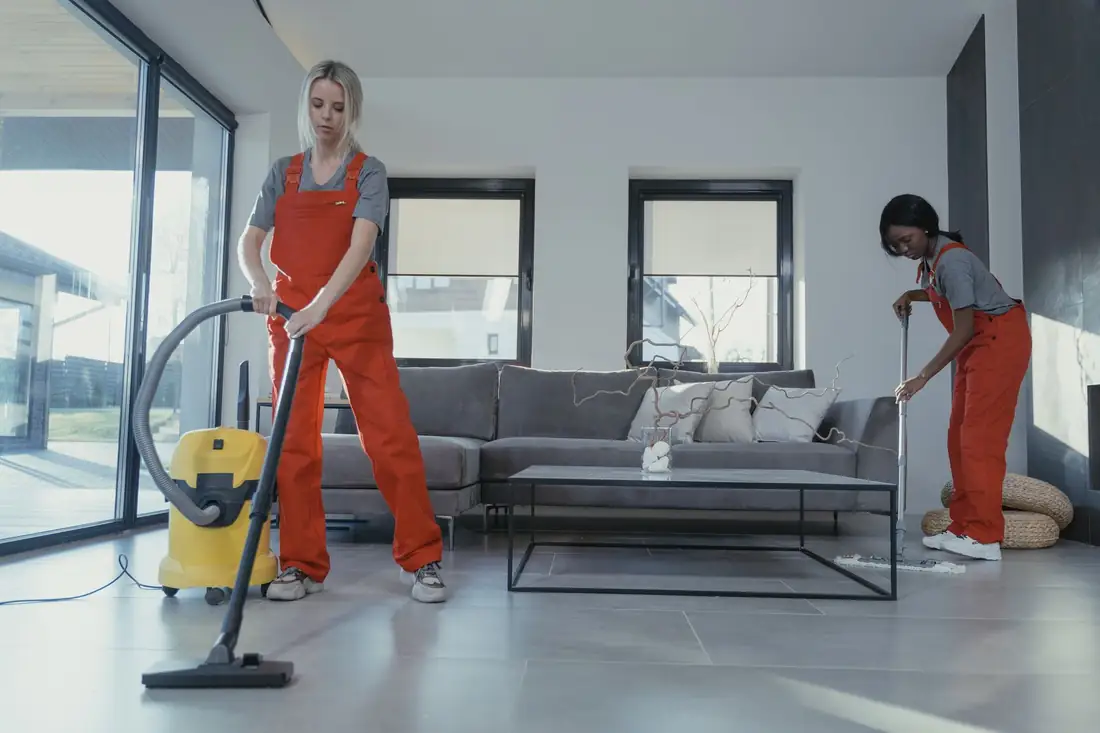 Uniformed cleaning professionals using an industrial wet-and-dry vacuum and mop in a living room