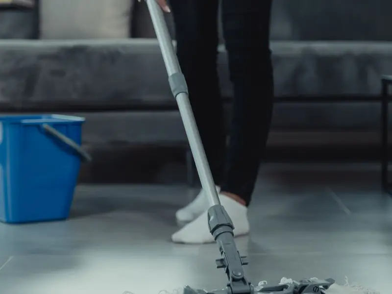 Cleaner mopping a tiled living room floor with a bucket nearby